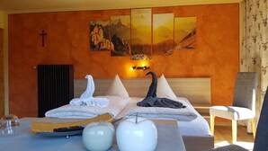 Une chambre d’hôtel avec un lit, un crucifix au mur et trois tableaux représentant des montagnes.