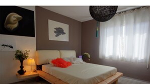 A bedroom with a wooden bed frame, a nightstand with a lamp, a vase with flowers, and a wall with a painting. - Art Apartment (Rovinj)