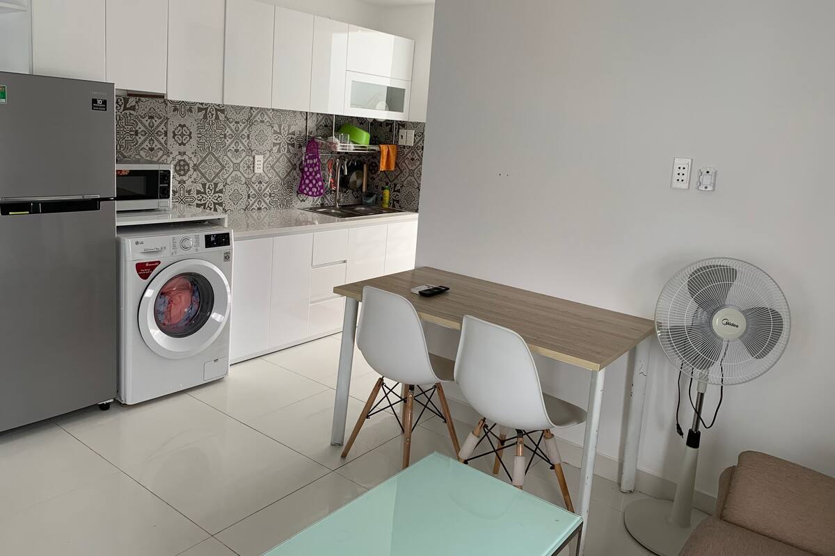 A modern kitchen with white cabinets, a built-in washing machine, a microwave, and a dining area with a table and chairs.