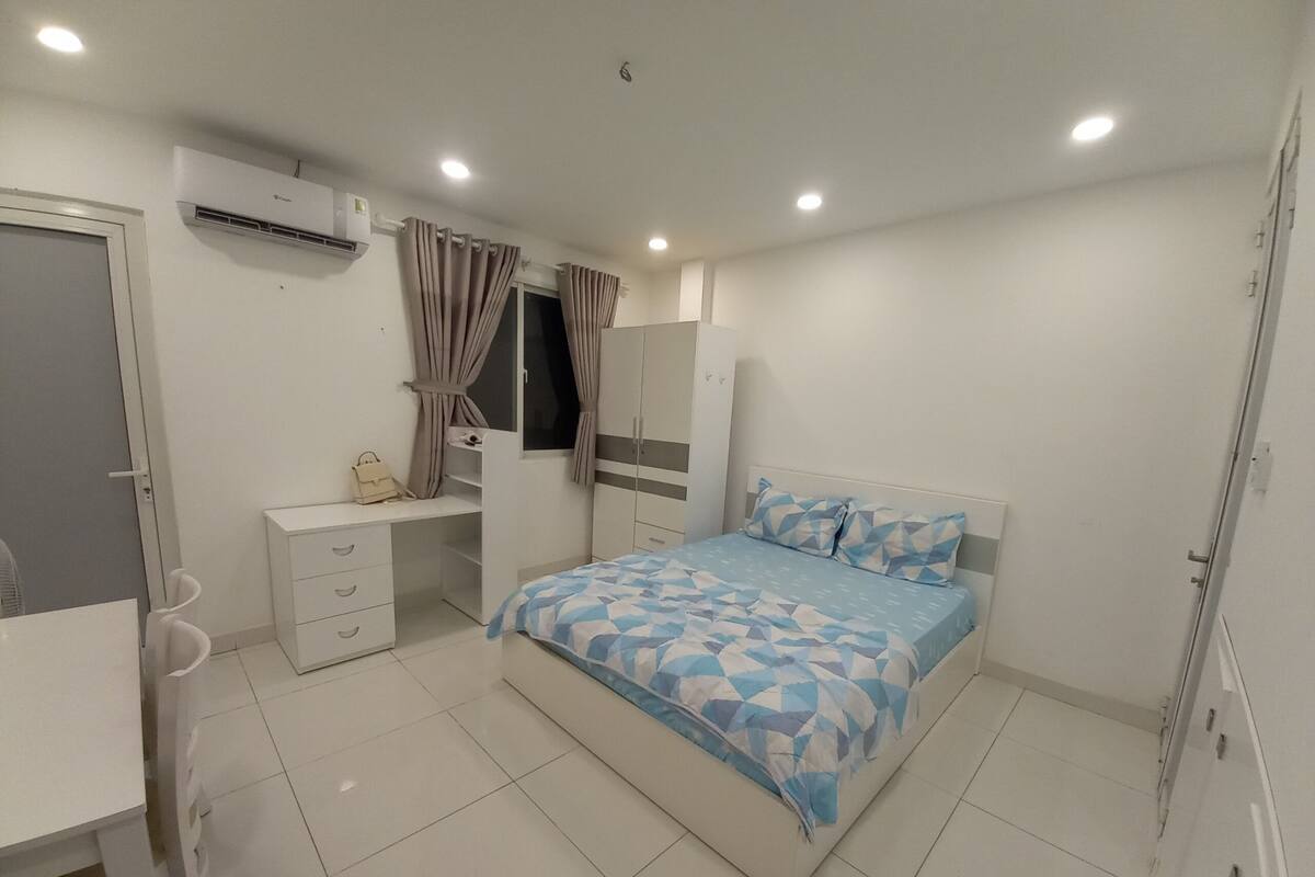 A bedroom with a bed, a desk, a wardrobe, and an air conditioning unit.