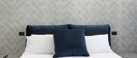 Een keurig opgemaakt bed met een combinatie van witte en donkerblauwe kussens, een hoofdbord en een behang met patroon.