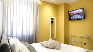 Una camera d'albergo con un letto, una televisione a muro, uno specchio e un pannello di vetro.