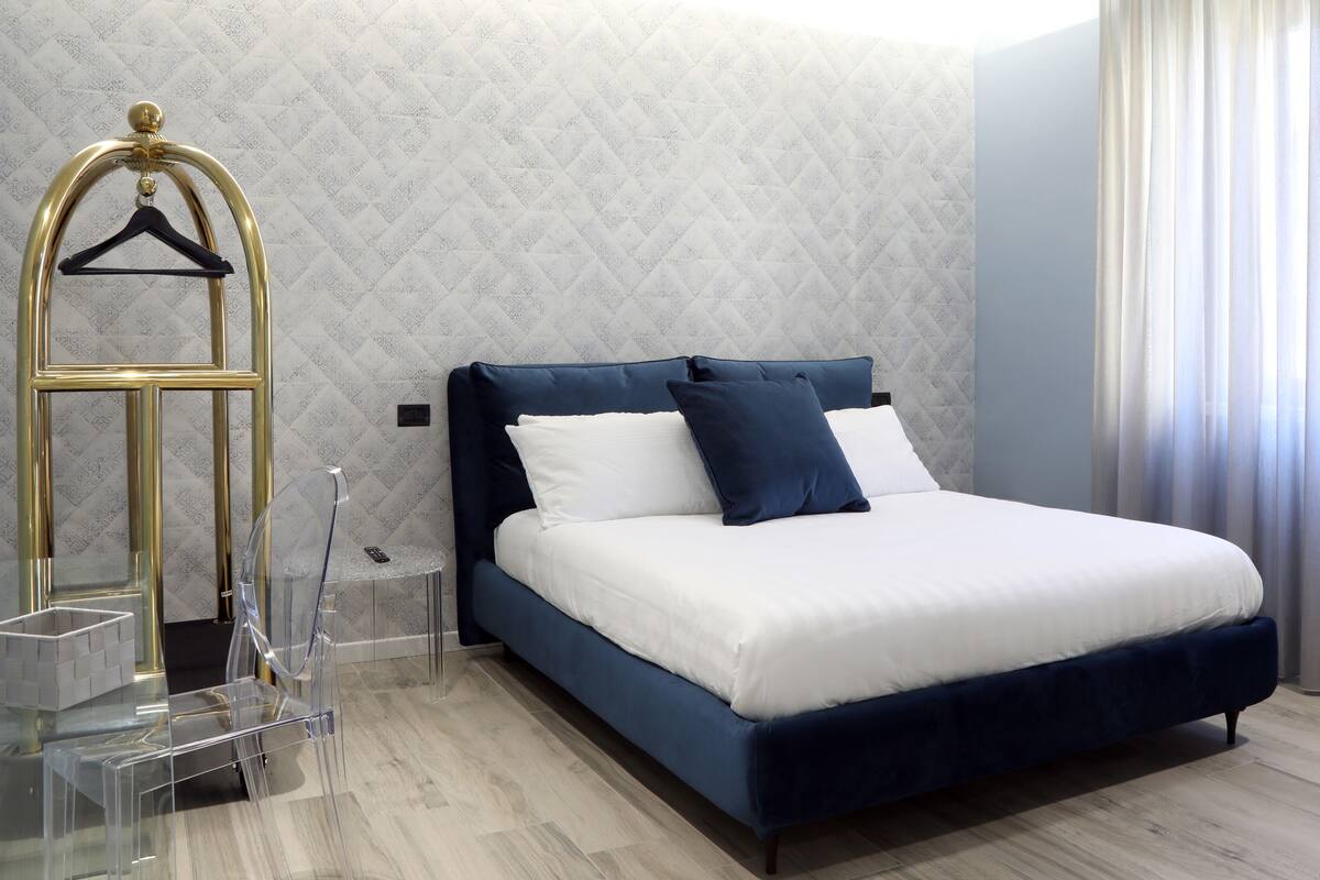 A modern hotel room with a large bed, a hanging coat rack, and a clear glass table.