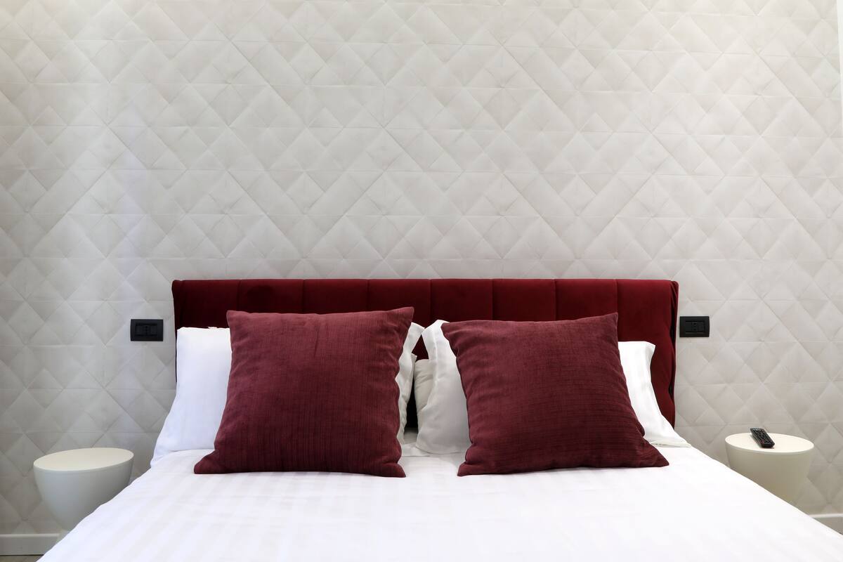 A bed with a red upholstered headboard, white bedding, and two red pillows.