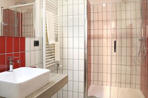 A modern bathroom with a white sink, a glass shower enclosure, and red-tiled walls.