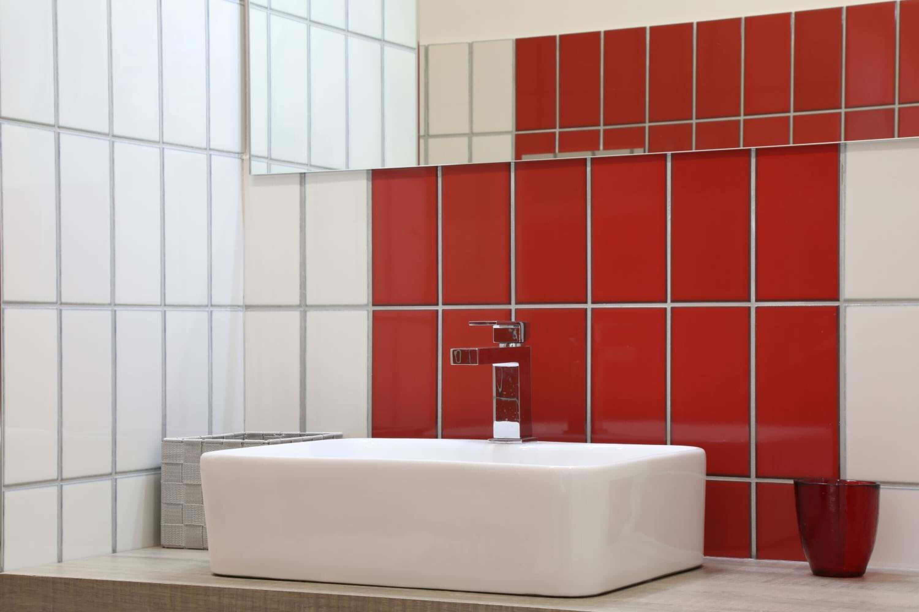 Un baño moderno con un lavamanos blanco, paredes con azulejos blancos y rojos, y un grifo de cromo.