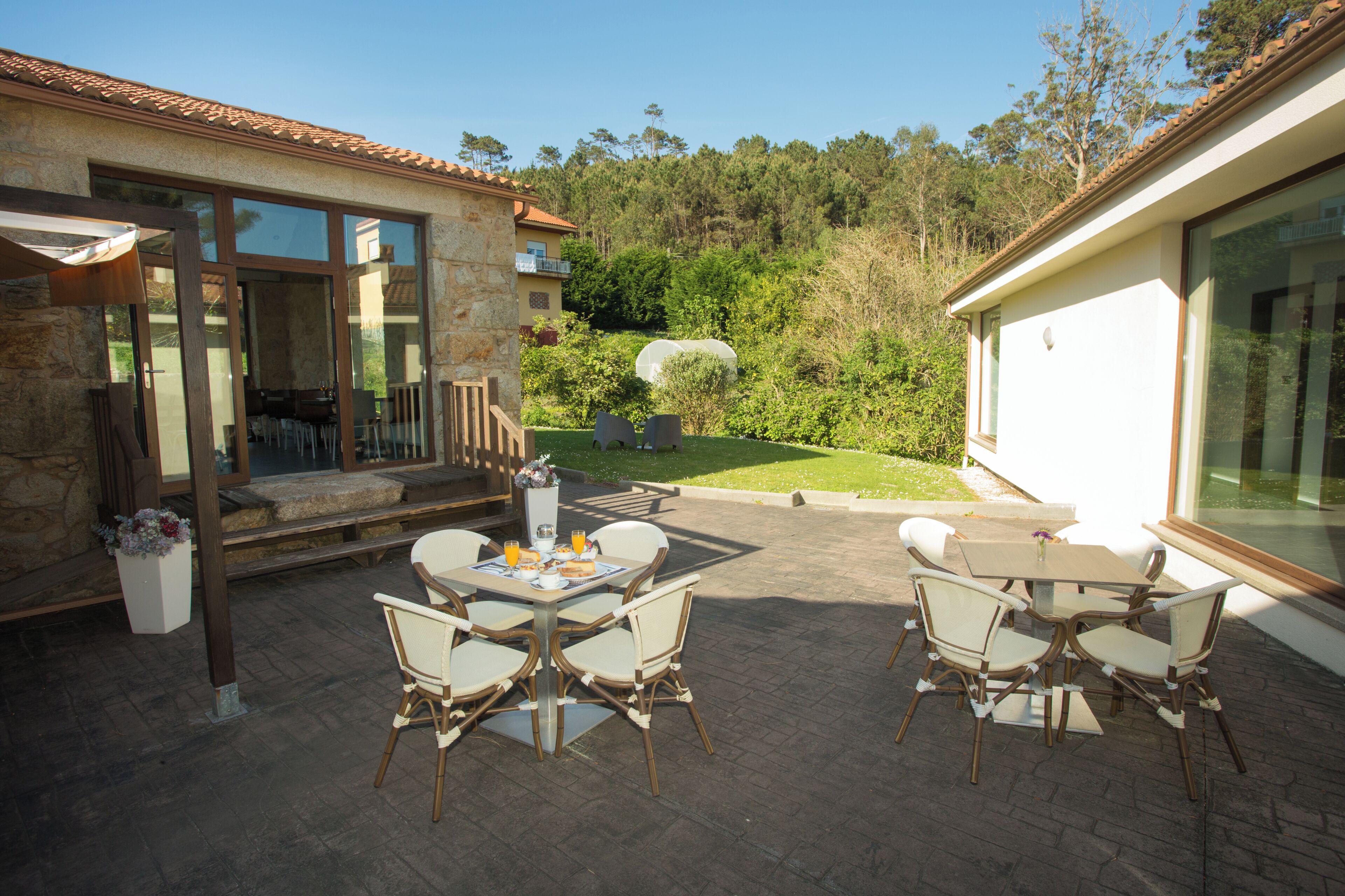 An outdoor patio with a table and chairs, a stone wall, and a view of a forested hillside.