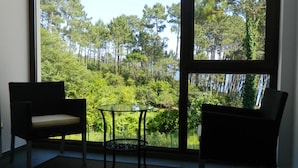 A room with a large window offering a view of a forest. There are two chairs and a small table in the room. - Hotel Alén do mar (Fisterra)