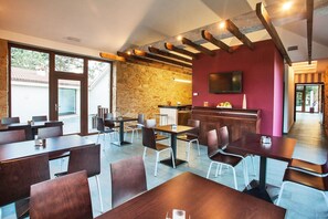 A modern dining area with wooden tables and chairs, a stone wall, and a television mounted on the wall. - Hotel Alén do mar (Fisterra)