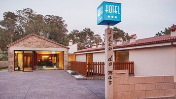 Entrada de un hotel con fachada de piedra, valla de madera y un cartel.