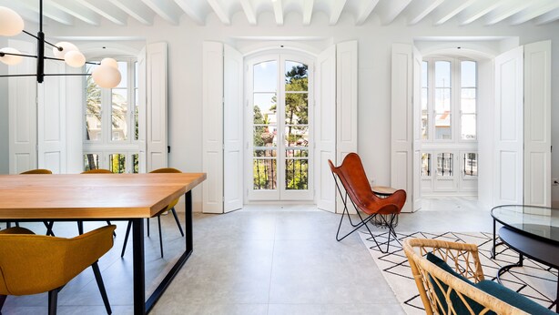 Uma sala de jantar espaçosa com uma mesa de madeira comprida e cadeiras modernas, portas brancas que dão para uma varanda e teto com vigas aparentes.