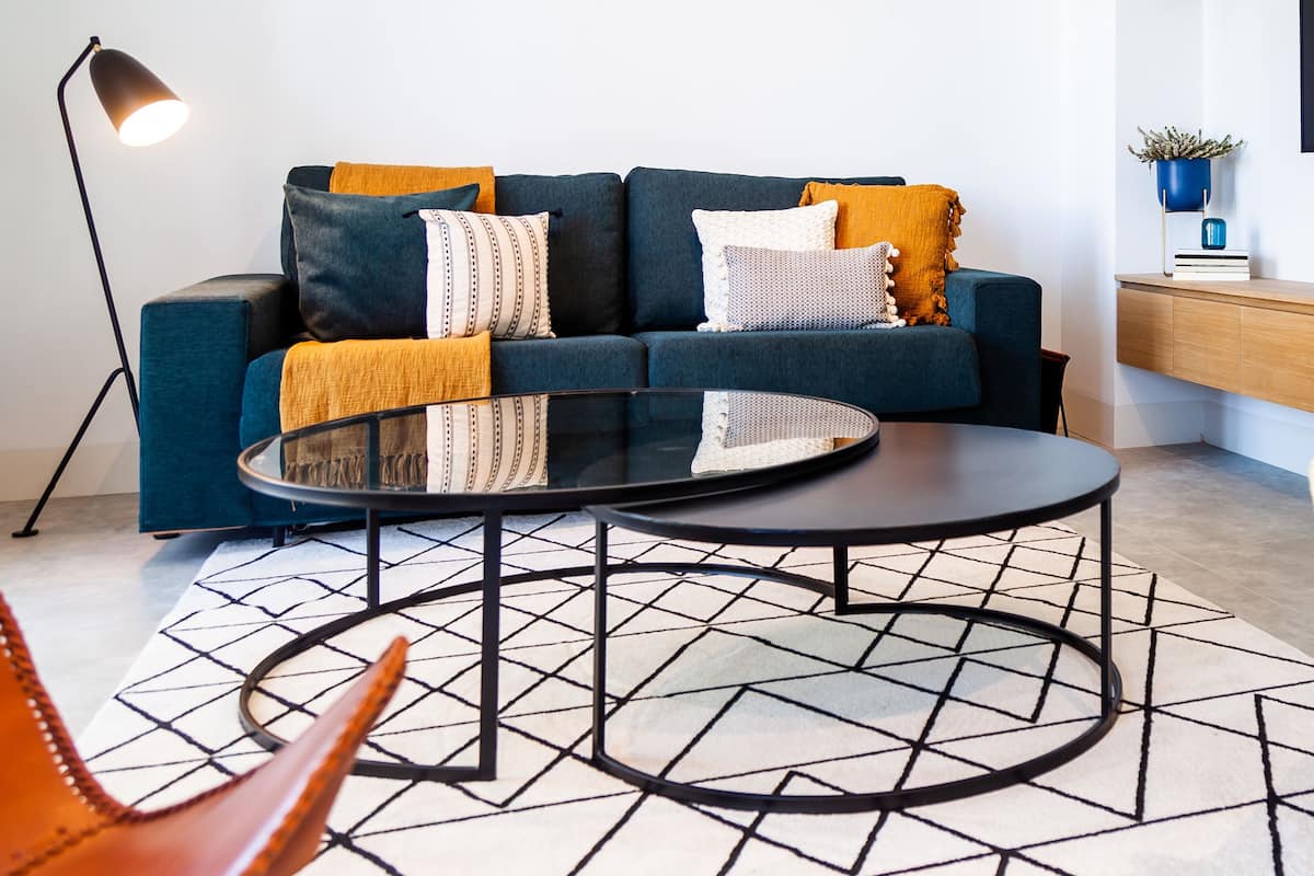 A modern living room with a sofa, a round coffee table, a wicker chair, and a floor lamp.