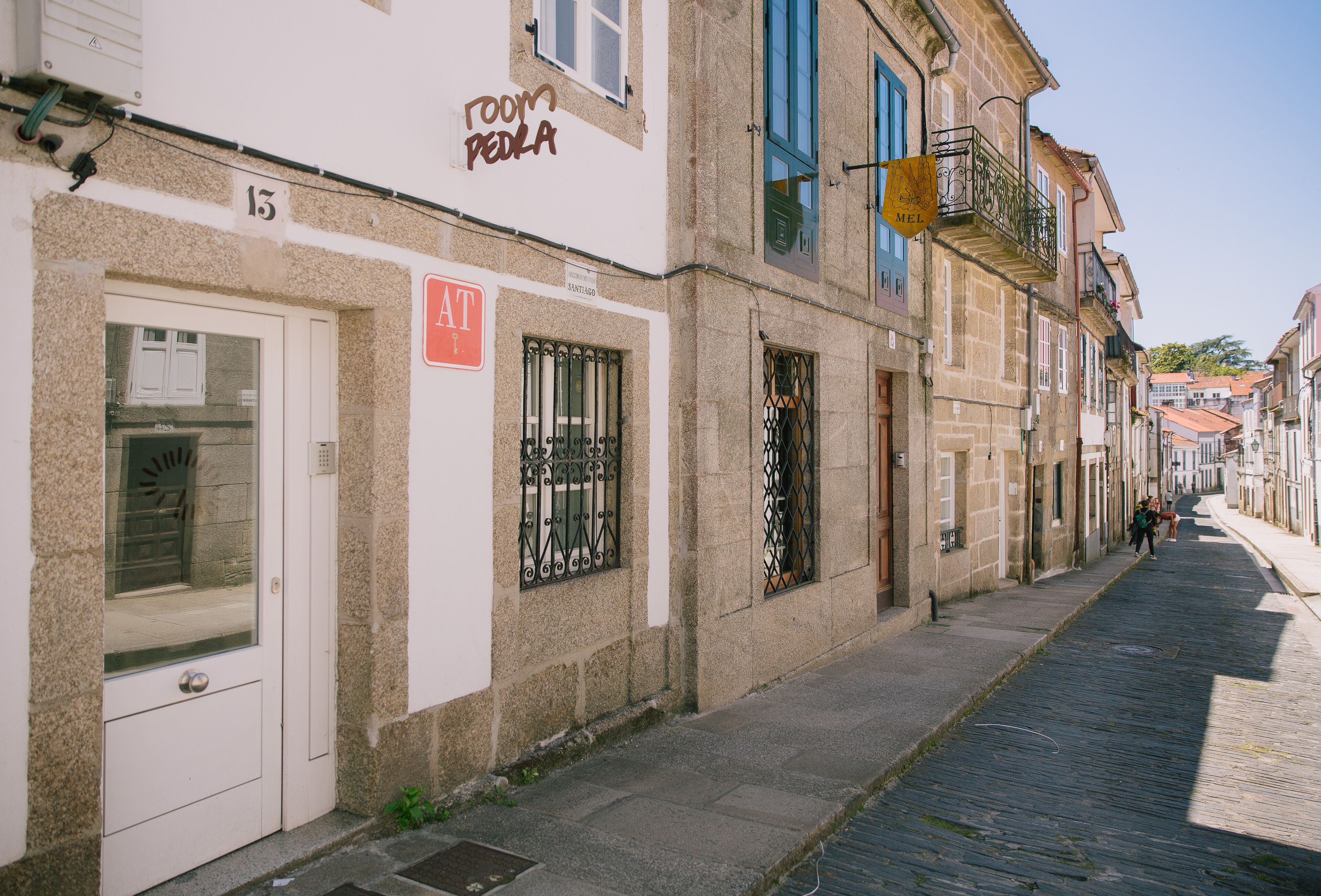 Une rue étroite bordée de bâtiments historiques, dont un hôtel avec une enseigne indiquant « Chambre PEDRA » et un numéro de porte bien visible, le « 13 ».