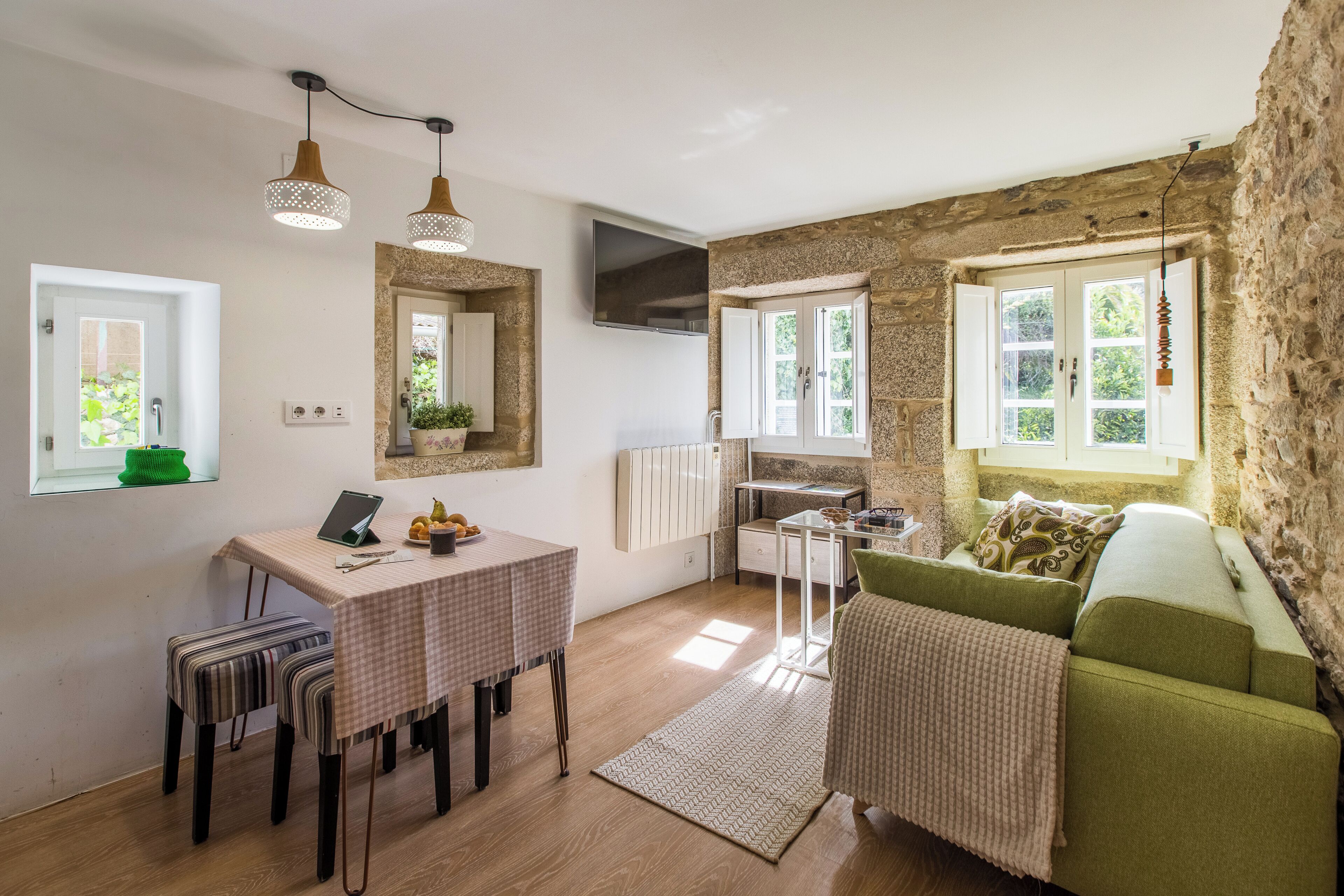 Una sala acogedora con un sofá verde, una mesa de comedor con sillas, una zona de cocina y una pared de piedra.