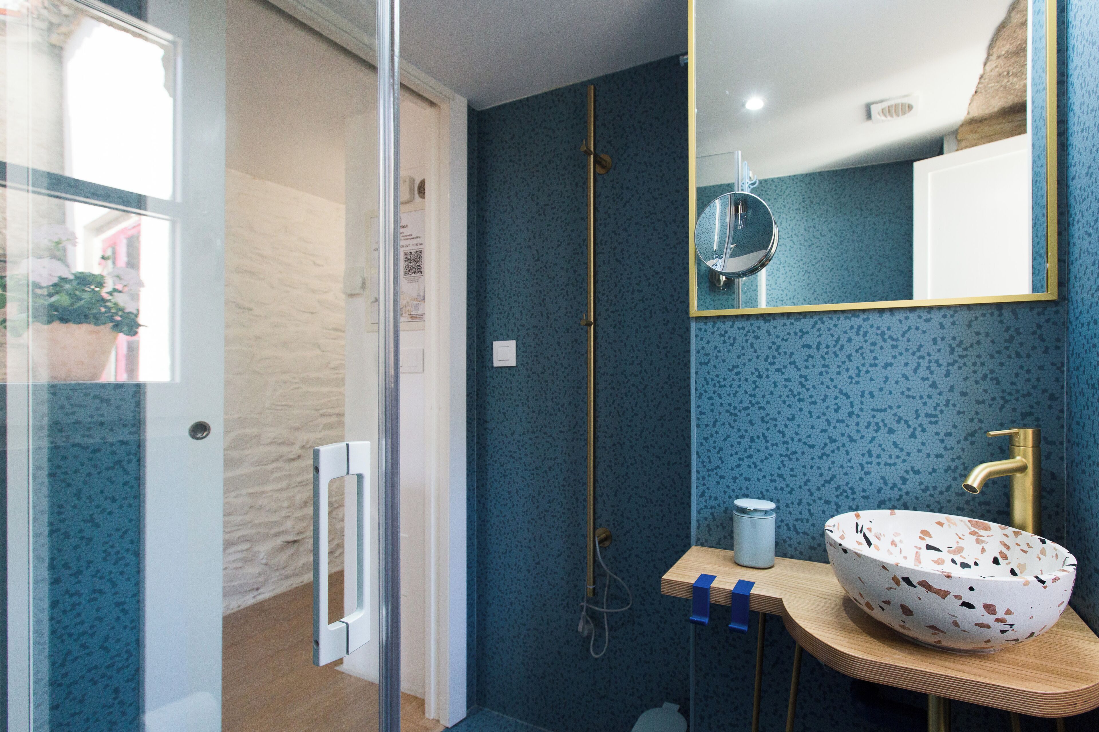 A bathroom with a blue speckled wall, a wooden vanity, a white bowl sink, a gold faucet, and a mirror with a gold frame.