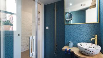 A bathroom with a blue speckled wall, a wooden vanity, a white bowl sink, a gold faucet, and a mirror with a gold frame.