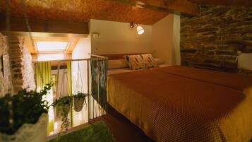 A bedroom with a wooden ceiling, a stone wall, a bed with a brown blanket, and a hanging plant.