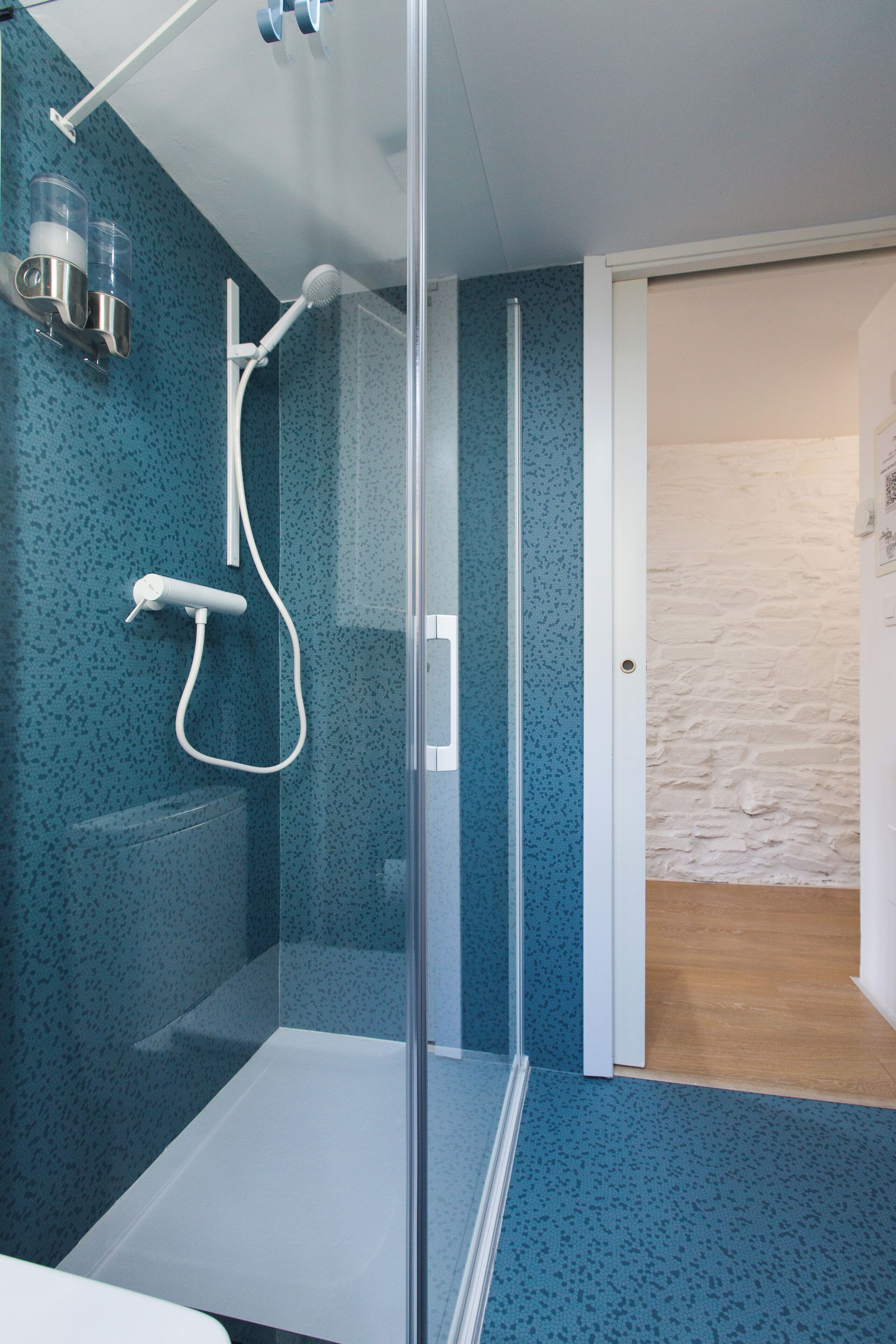 Un baño moderno con cabina de ducha de vidrio, un lavamanos blanco y una pared azul con salpicaduras.
