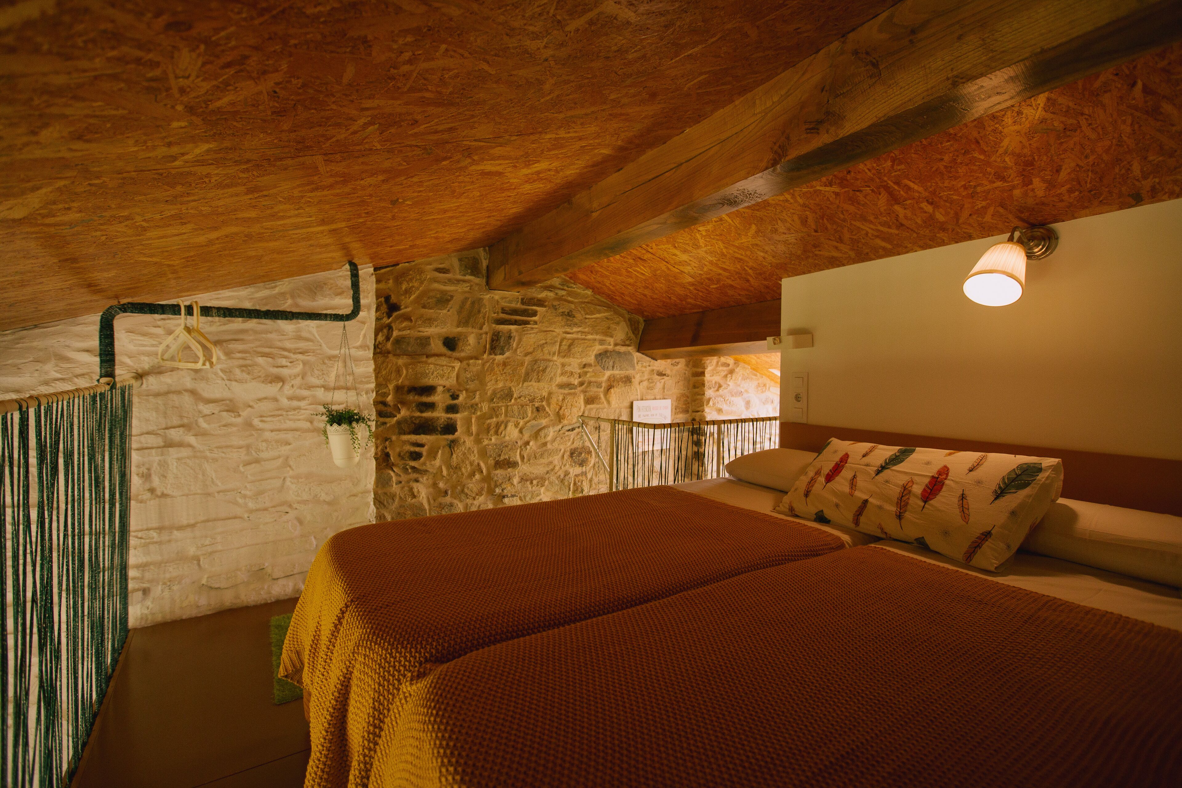Una habitación acogedora con pared de piedra, vigas de madera, cama con un cojín estampado y una planta colgante.