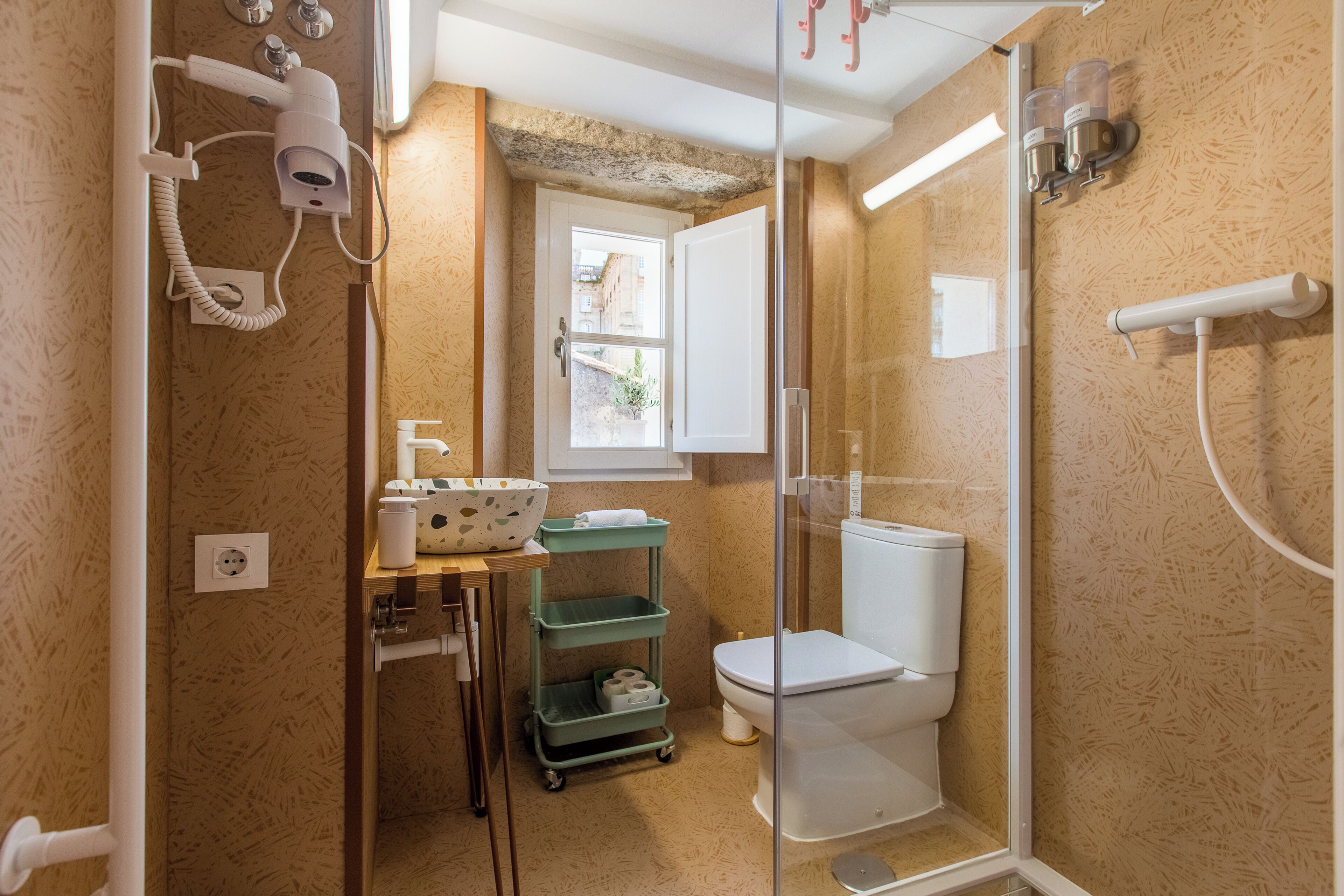 Un baño con cabina de ducha de vidrio, inodoro, lavabo y una pequeña ventana.