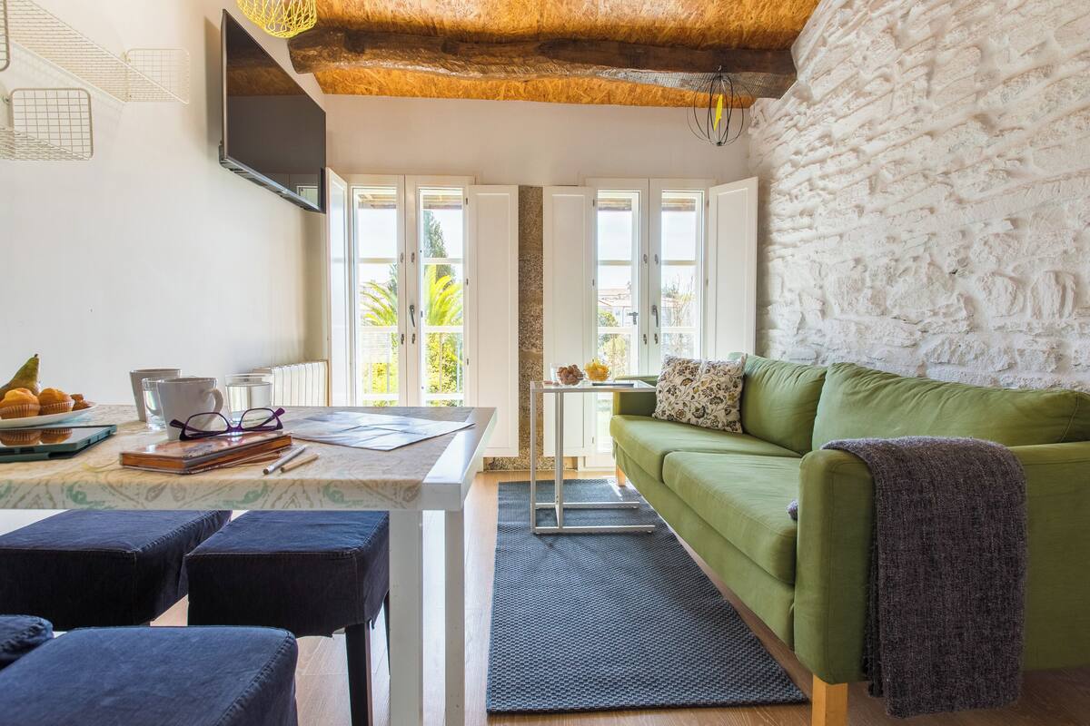 Un salon chaleureux avec un canapé vert, une table basse et un téléviseur fixé au mur.