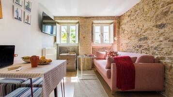 Una sala de estar acogedora con una pared de piedra, un sofá rosa, una mesa de comedor con una computadora portátil y un televisor montado en la pared.