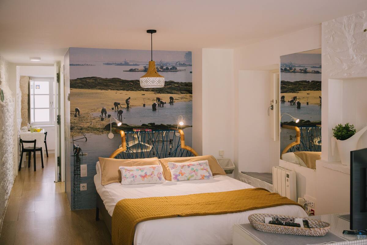 Une chambre avec un lit, un bureau, une chaise et une grande fresque murale représentant une plage.