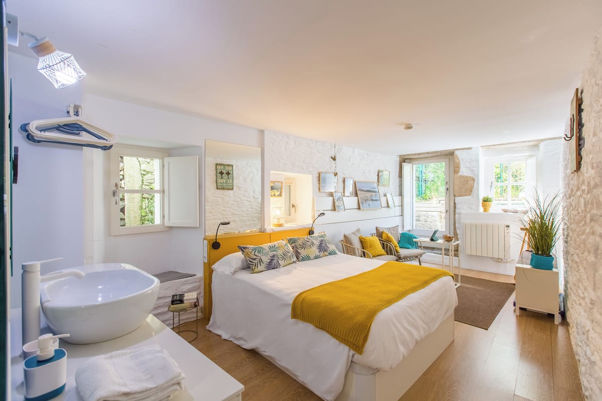 Une chambre avec un grand lit, une table de chevet, un lavabo blanc et un miroir.