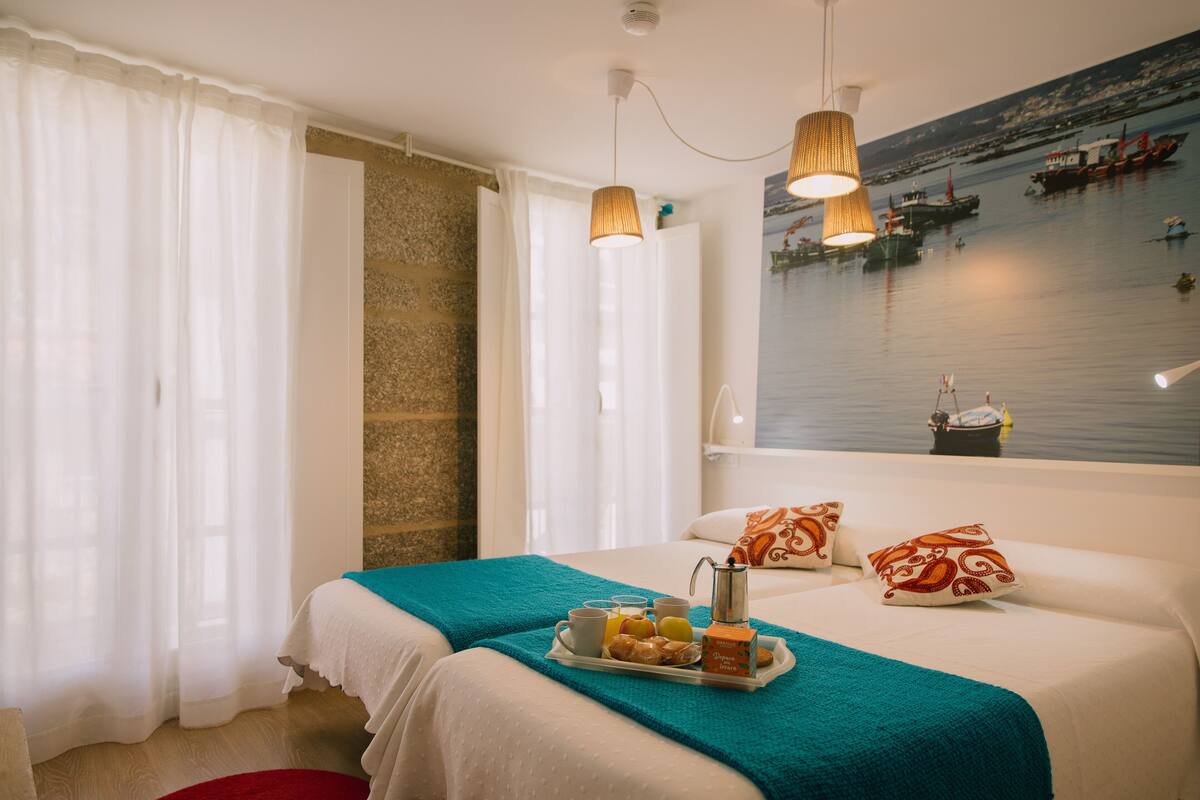 Une chambre d’hôtel avec un lit, un plateau de petit-déjeuner, une fenêtre donnant sur le port et une peinture représentant un paysage marin.