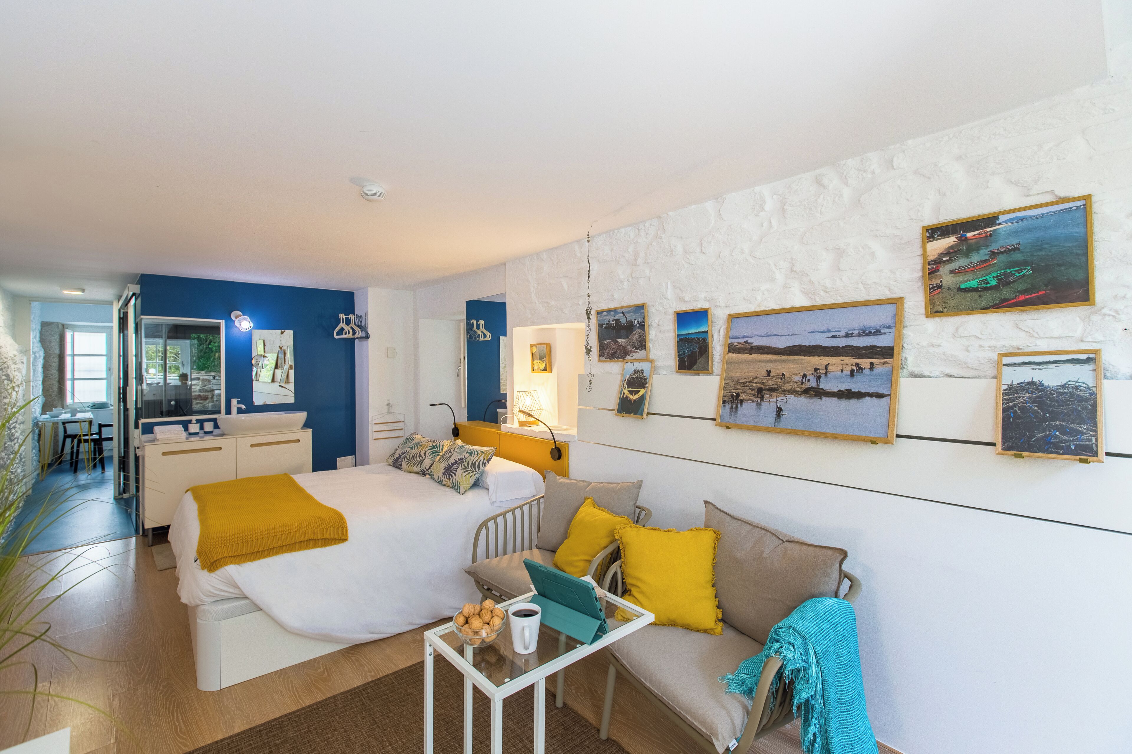 A hotel room with a bed, a sofa, a small table with a cup and cookies, a mirror, and a wall with framed pictures.