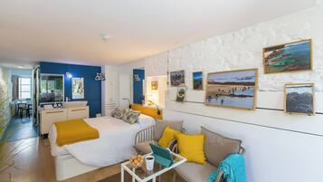 A hotel room with a bed, a sofa, a small table with a cup and cookies, a mirror, and a wall with framed pictures.