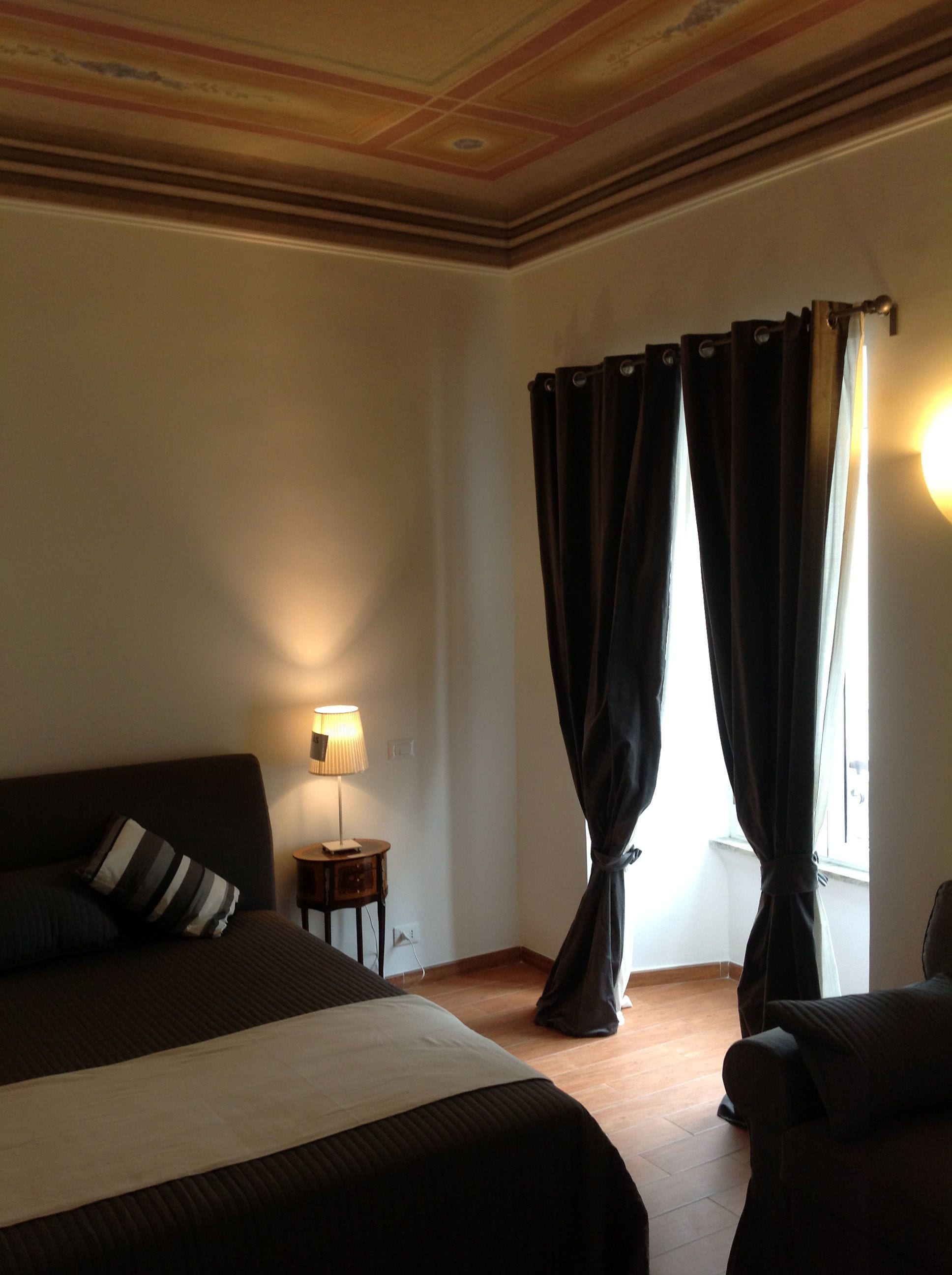 A hotel room with a large bed, a bedside table with a lamp, and a window with curtains.