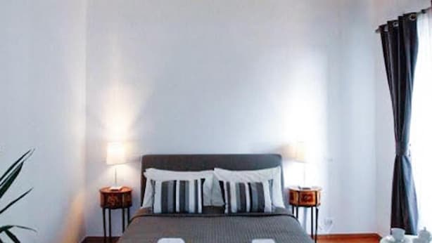 Habitación de hotel con una cama grande, dos mesitas de noche, una lámpara de noche, una planta en maceta y un techo decorativo.