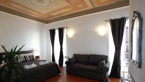 Habitación de hotel con cama, sofá, planta en maceta y espejo.