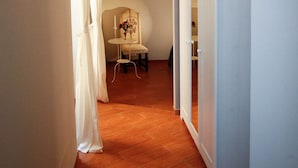 Un pasillo estrecho con suelo de madera, un armario blanco y una mesa con una silla.