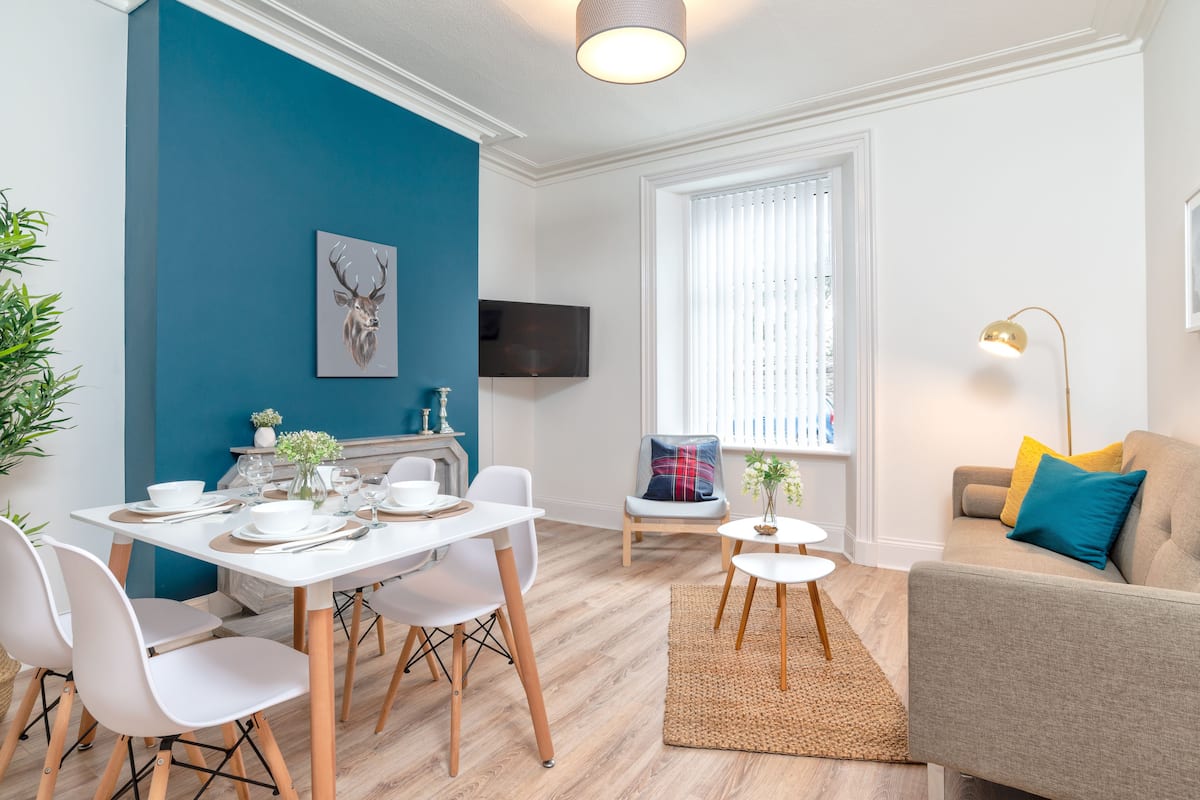 A modern living room with a dining area, a sofa, a television, and a blue accent wall.