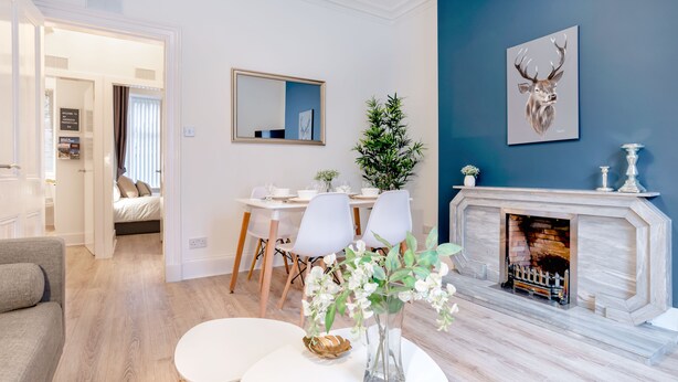 A modern living room with a fireplace, a dining area, and a bedroom visible through an open door. - West Mount Apartment (Aberdeen)