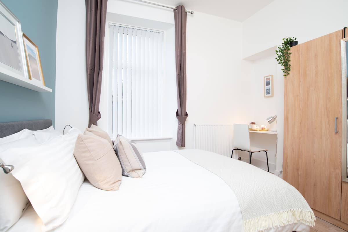 A bedroom with a bed, a desk, a wardrobe, and a window with curtains.
