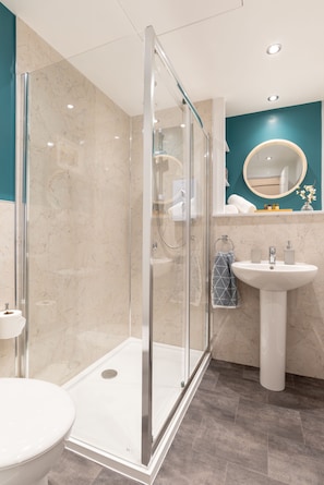 Enjoy a refreshing shower in the glass-enclosed shower area with a pedestal sink and large mirror.