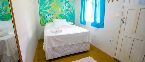 Un dormitorio con cama, espejo, decoración temática tropical, ventana con cortinas azules y una puerta.
