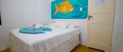A single bed with white bedding, a blue blanket, and rolled towels. A painting of a fish is on the wall.
