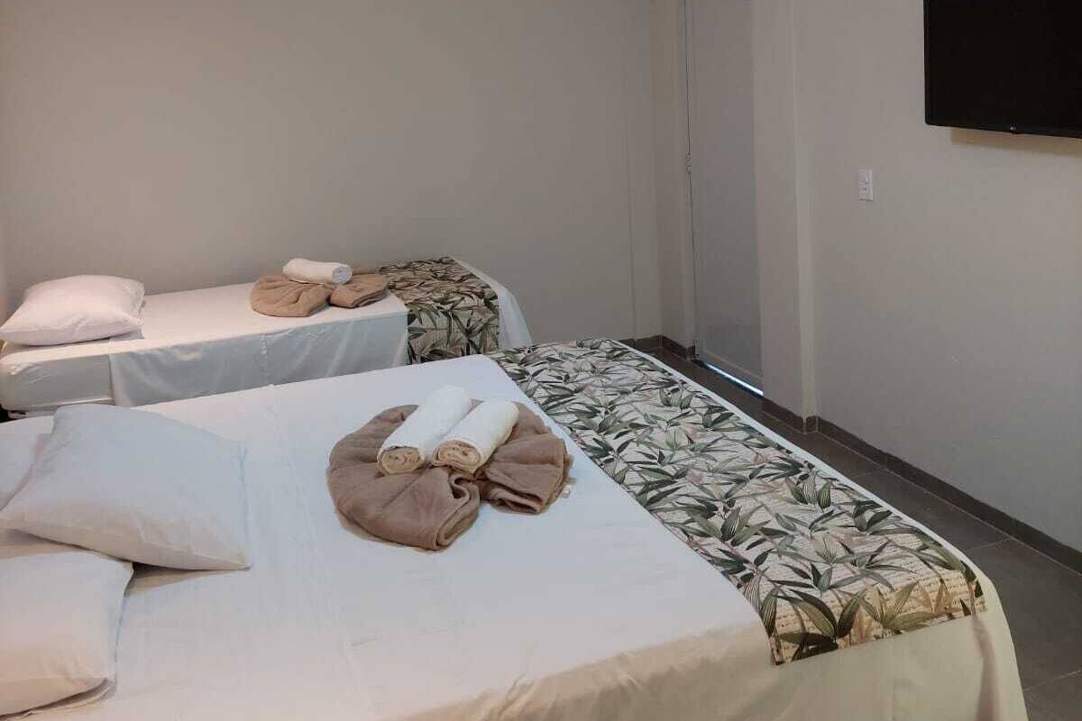 A hotel room with two beds, each with a pillow and a towel. There is a television mounted on the wall.