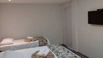 Quarto de hotel com duas camas, cada uma com travesseiro e toalha. Há uma televisão fixada na parede.