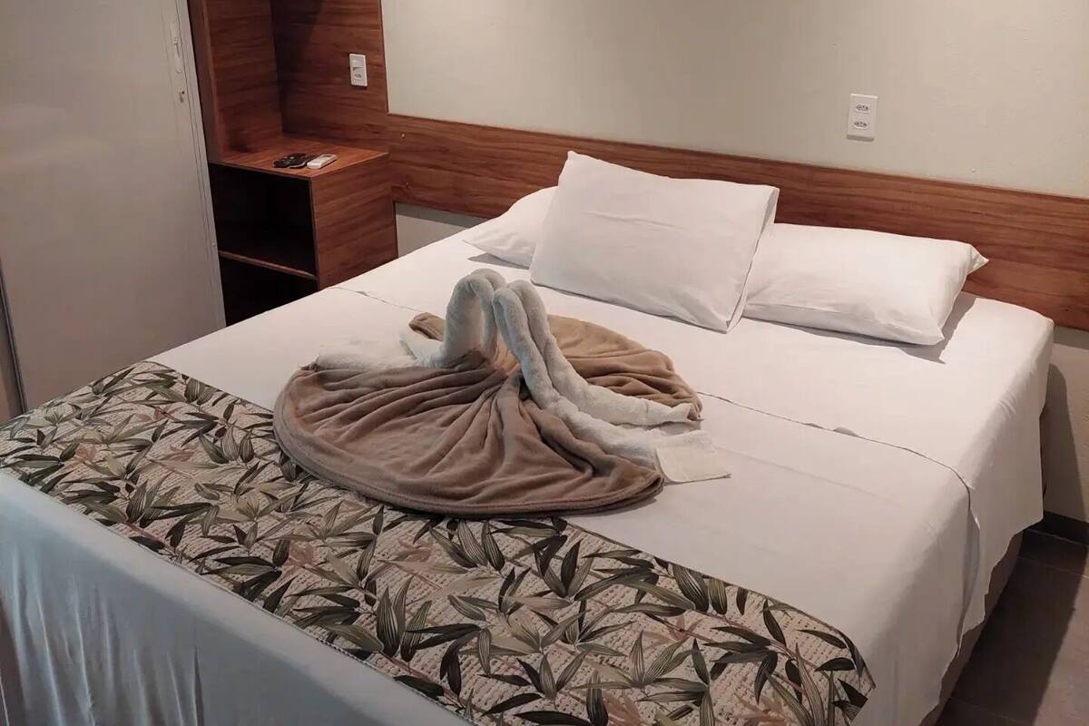 A hotel room with a bed, a wooden headboard, a wardrobe, and a small table with a remote control.