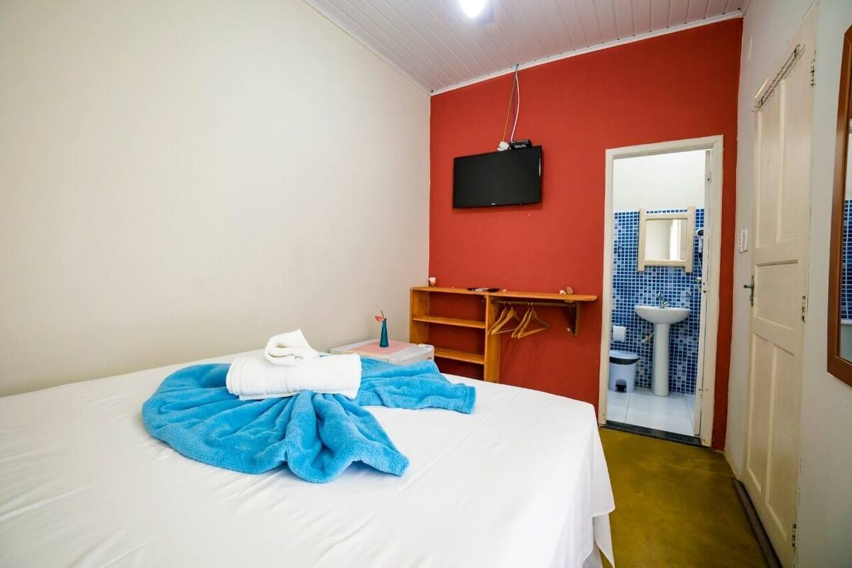 A hotel room with a bed, a television, a bathroom with a sink and mirror, and a red wall.