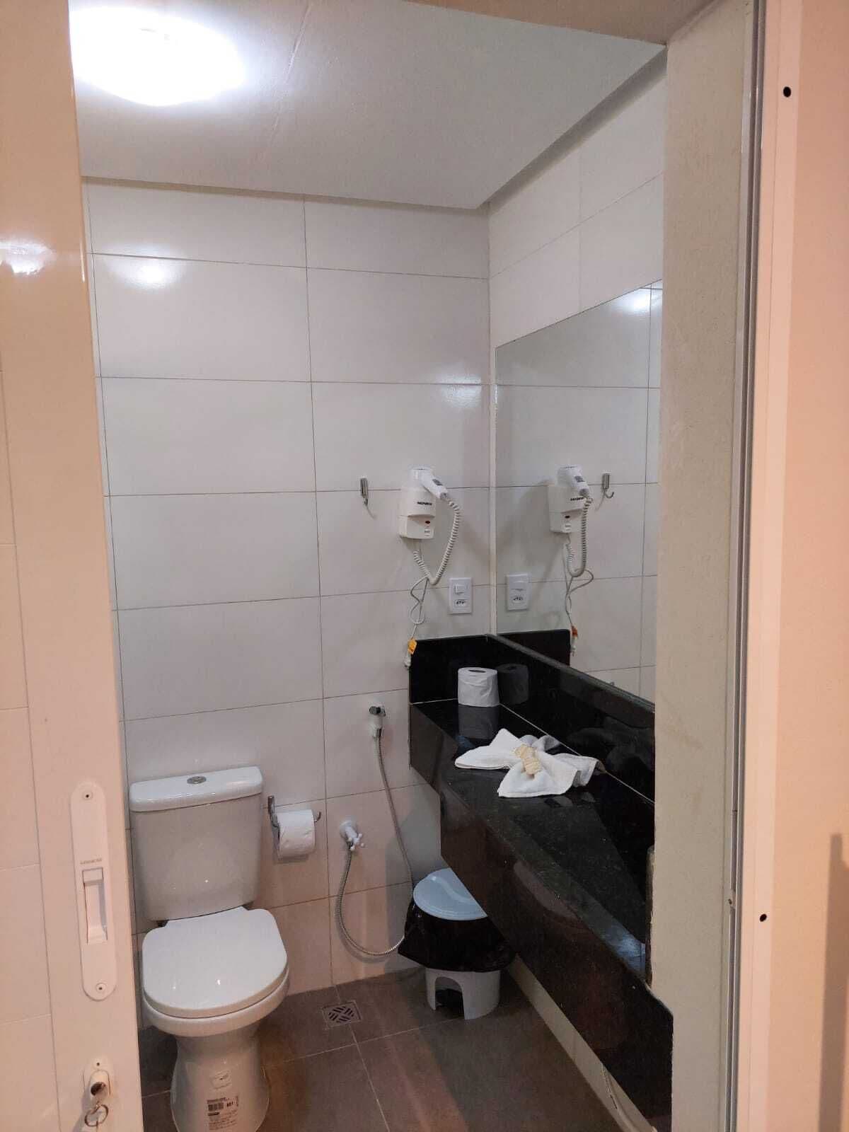 A small, tiled bathroom with a toilet, a sink with a mirror, and a hairdryer on the wall.