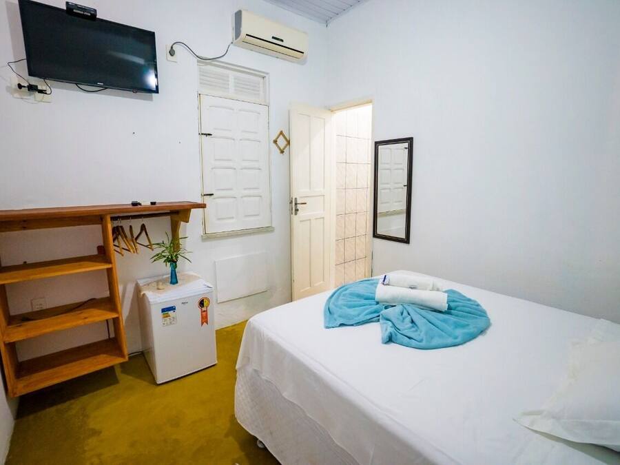 A bedroom with a bed, a TV, a small refrigerator, a wooden shelf, and a door.