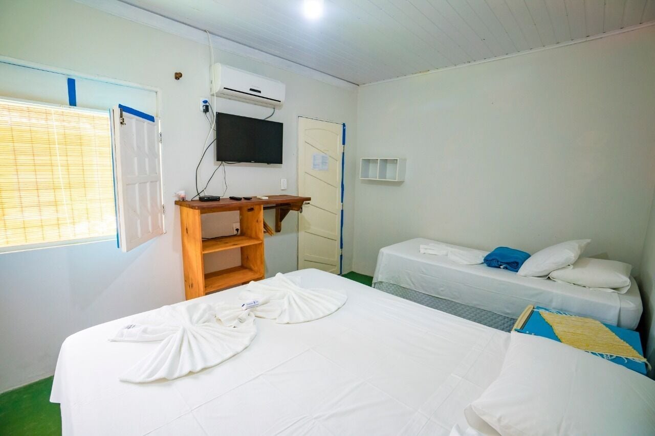 A hotel room with two beds, a TV, a desk, and a window with blinds.