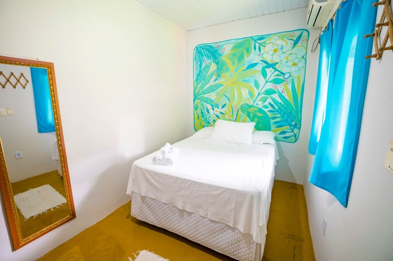 Habitación con una cama individual, un espejo grande, un cabecero con motivos tropicales y una cortina azul.
