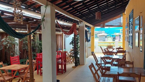 A spacious indoor area with wooden tables and chairs, a hanging light fixture, and a view of the outdoors. - Pousada Sunset Boipeba (Cairu)